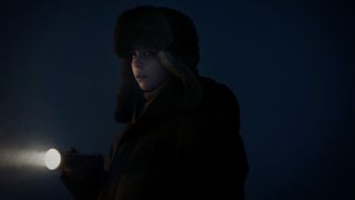 Young girl wrapped up in a warm winter hat and coat holding a flashlight as she searches in the dark.