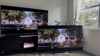 The LG G4 OLED TV on a TV bench, with LG G3 OLED next to it on the floor, and both showing the same scene from the opening of the movie A View to Kill