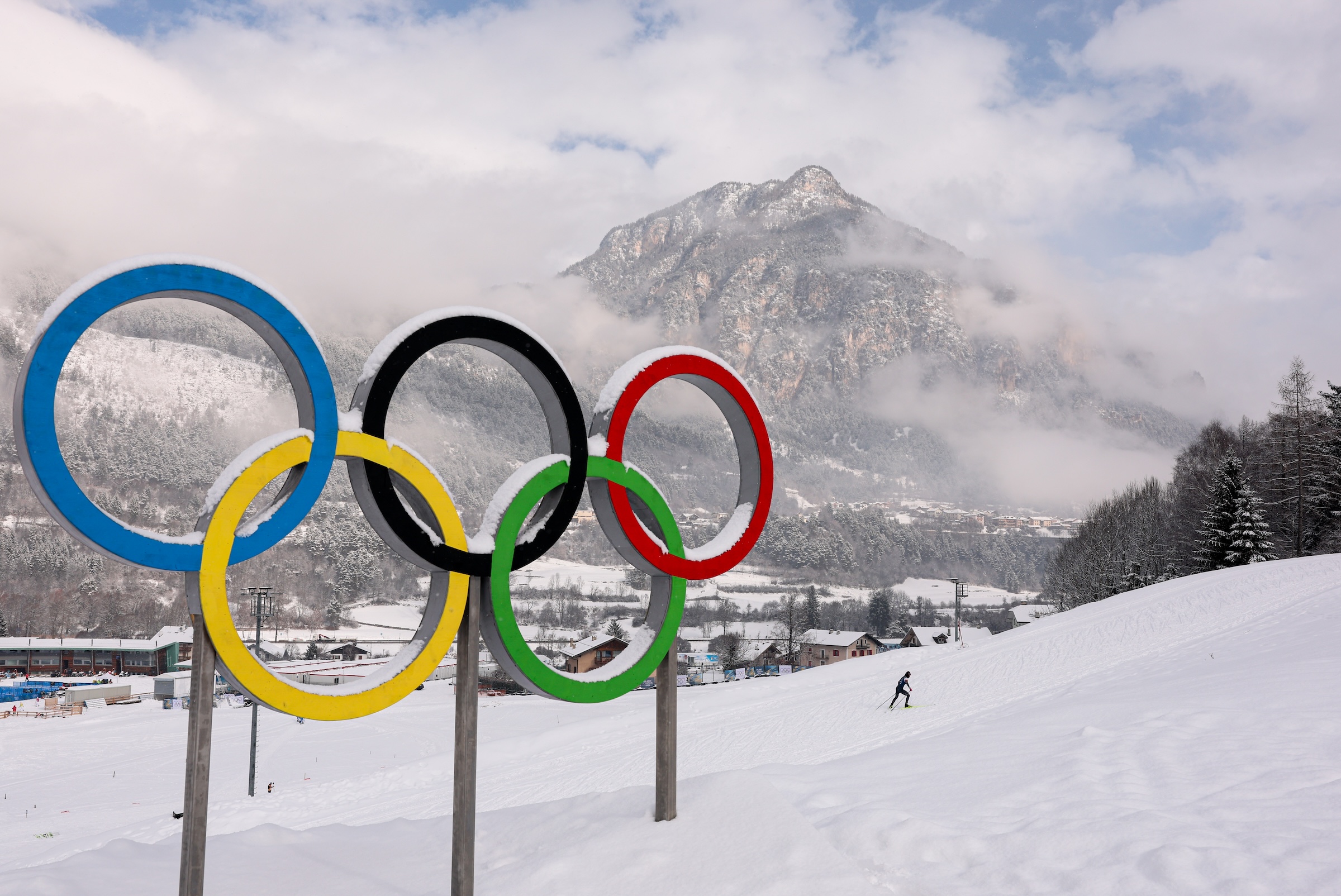 A metal statue of the Olympic rings in Italy in front of a snowy mountain