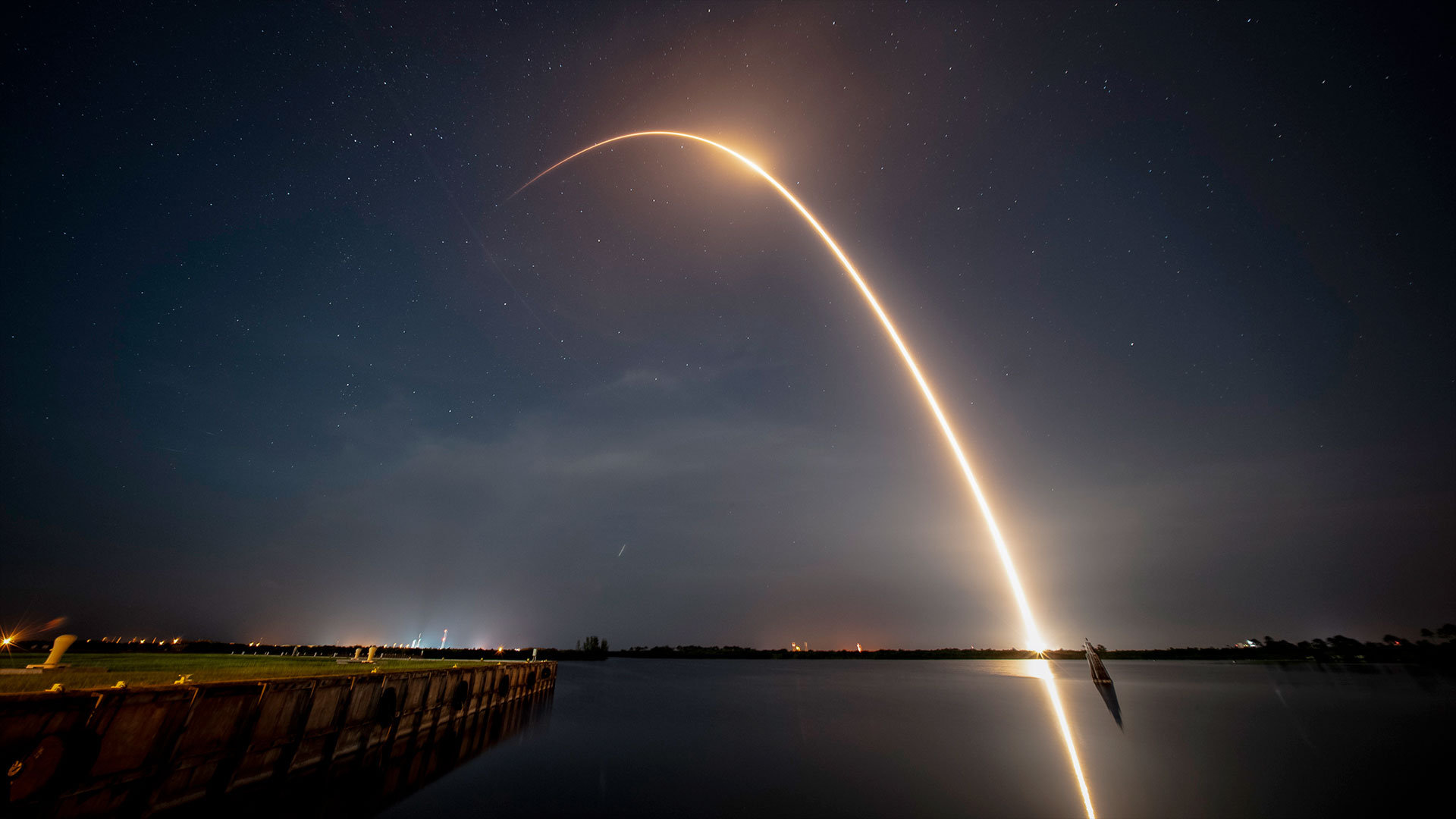 a timelapse exposure captures the arching streak of a rocket launching into space in the early morning, pre-dawn sky.