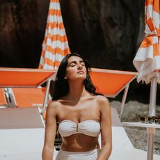 a woman with dark hair in a white bikini on a white and orange background