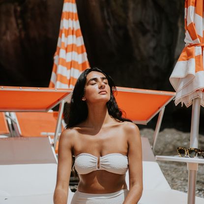 a woman with dark hair in a white bikini on a white and orange background