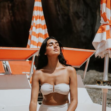 a woman with dark hair in a white bikini on a white and orange background