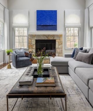 Living room with gray sectional and armchair, coffee table, fireplace and blue painting