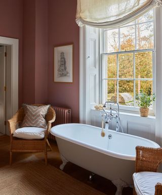 A traditional bathroom with pink walls, a roll top bath and wicker chair
