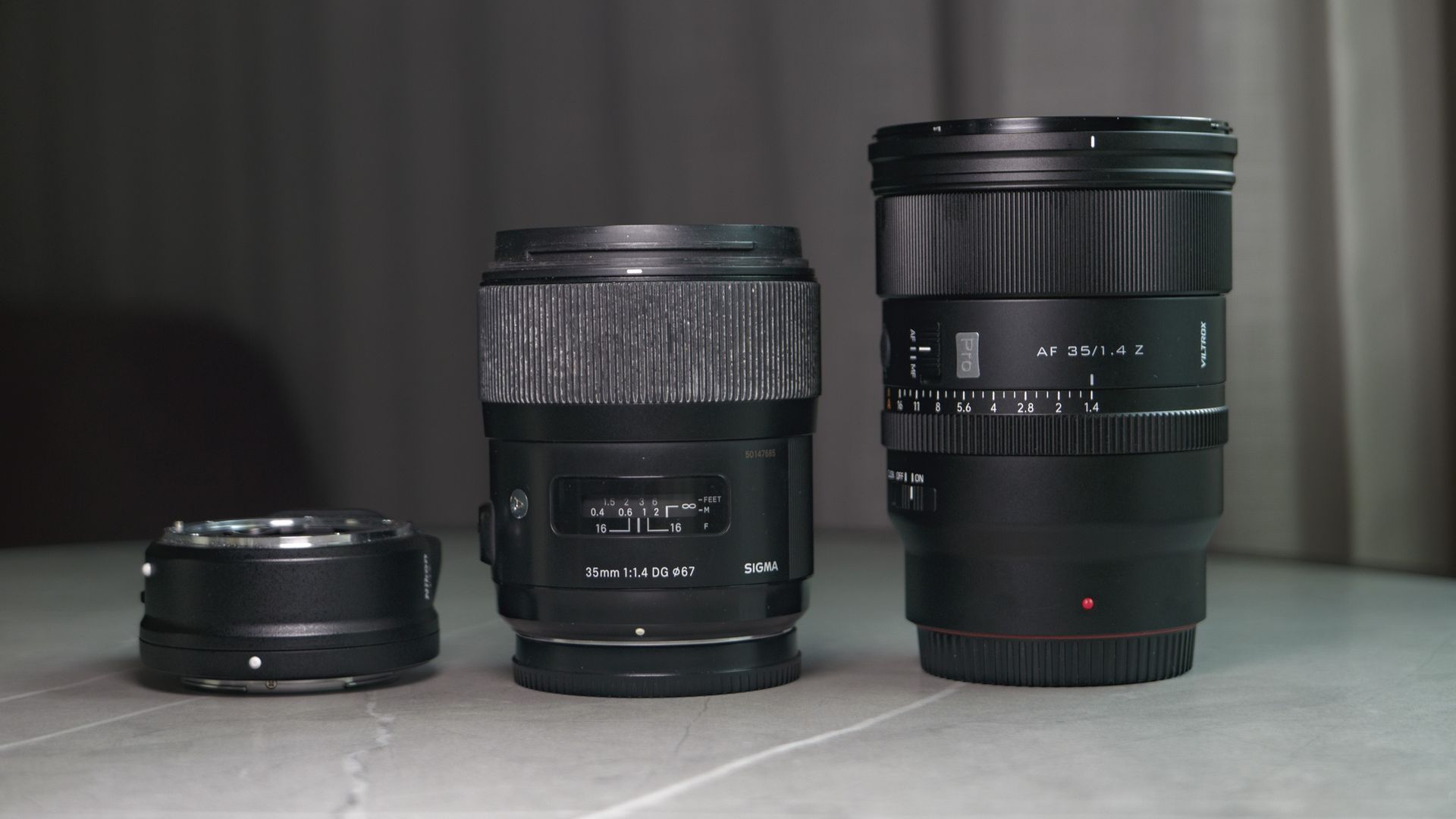 Viltrox AF 35mm F1.4 Pro lens alongside the Sigma 35mm f1/.4 DG Art lens, and the Nikon F to Z-mount adapter, on a white marble table