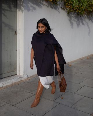 Woman wears black cape, white skirt and brown knee high boots