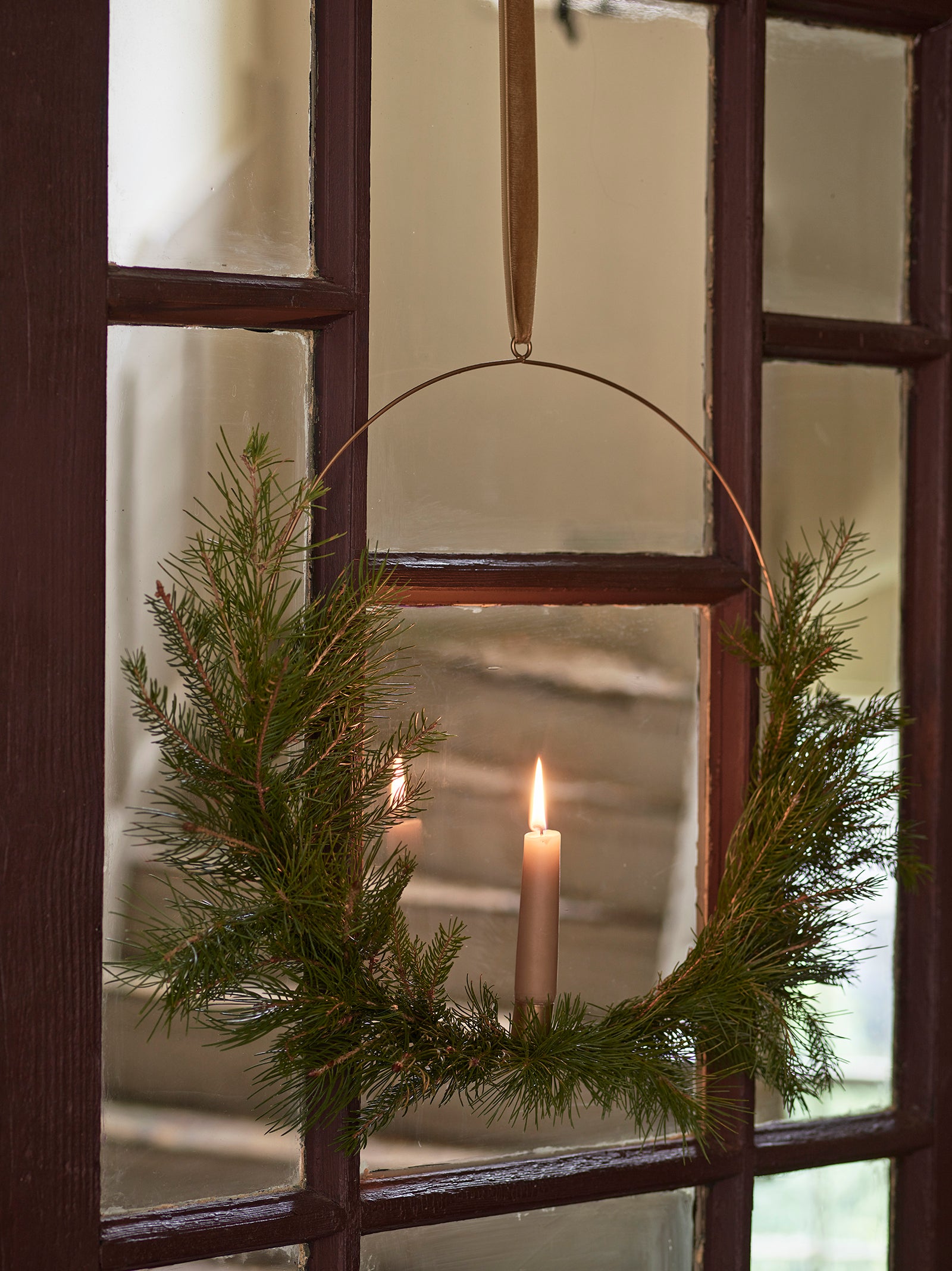 View through a glass door with a foliage wreath and lit candle, staircase in the background.