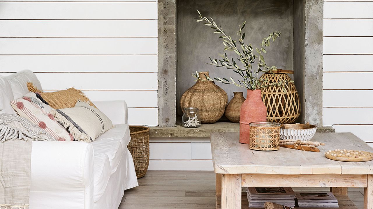 White sofa and wooden coffee table with vases in front of white panelled wall