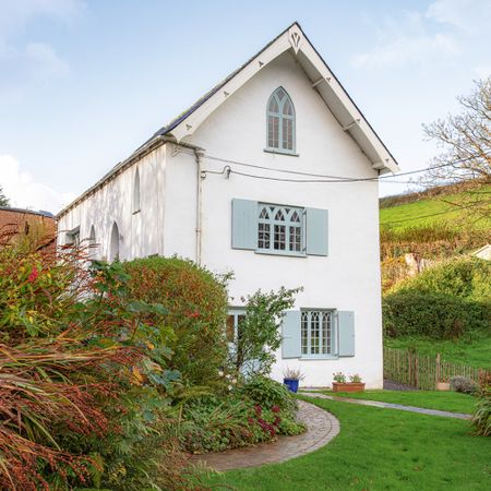 exterior of a whitewashed coastal cottage with gothic style arched windows and blue painted shutters