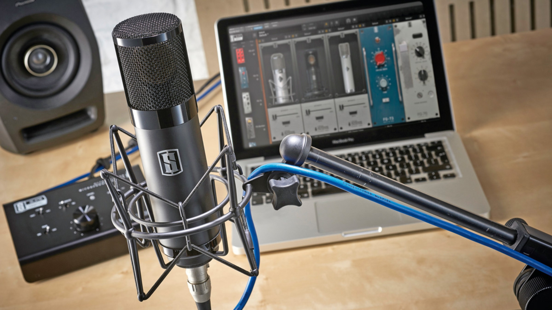 A Slate Digital VMS ML-1 XLR mic on a stand with a laptop, audio interface, and studio monitors in the background