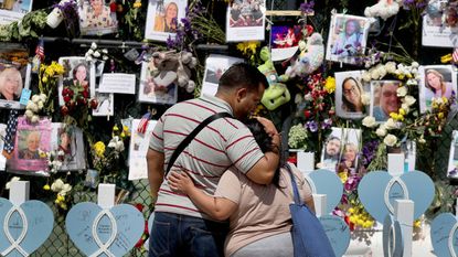 A couple hug as they look at pictures of victims of the collapsed 12-story Champlain Towers South condo building on July 8, 2021, in Surfside, Florida.