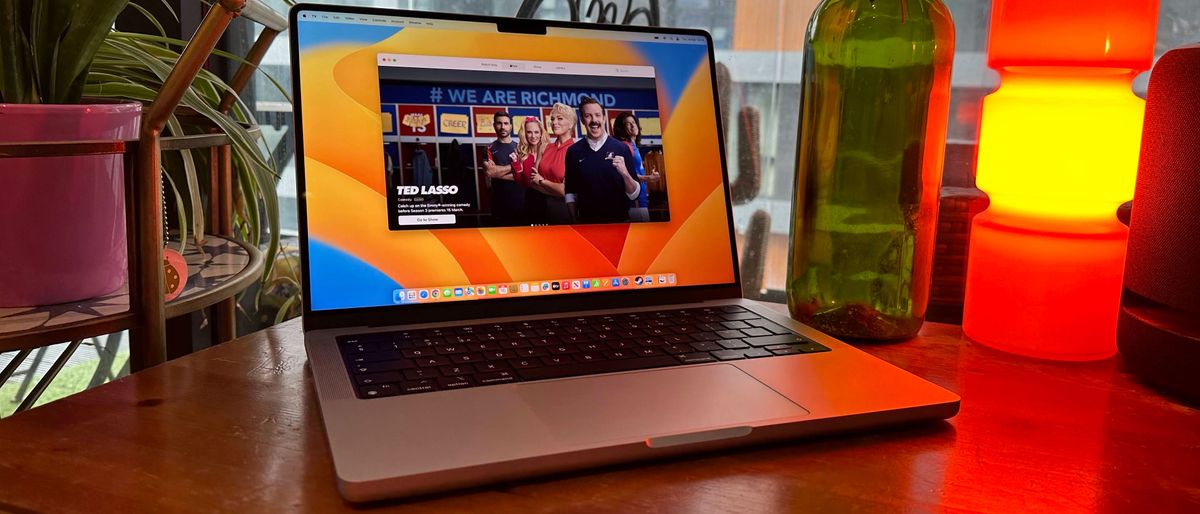 A 2023 14-inch MacBook Pro on a wooden counter, near a retro lamp.