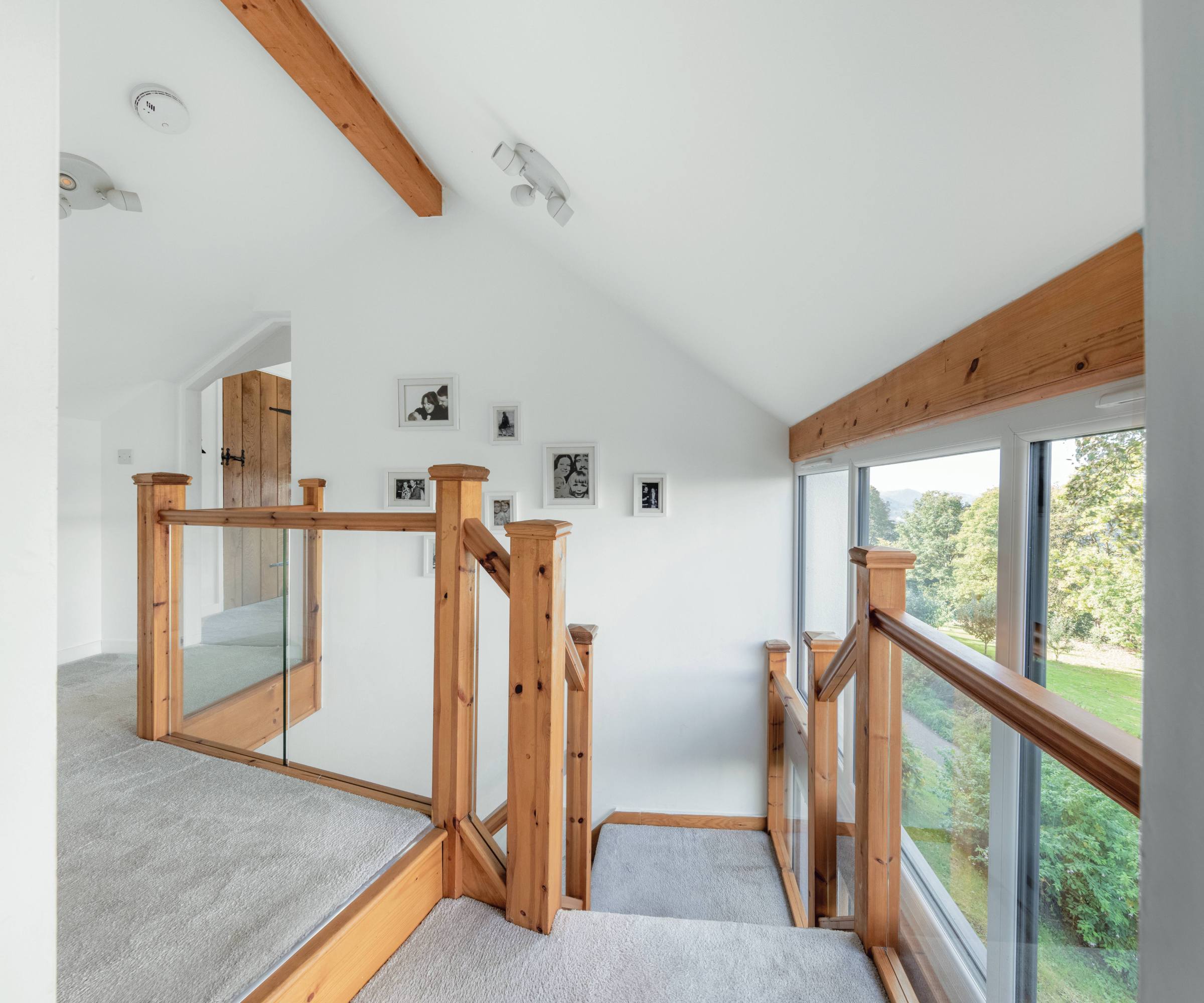 Wooden staircase landing grey carpet and exposed ceiling beams with full-height windows