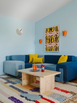 Tonal blue denim sofa against light blue wall with orange sconces and yellow artwork
