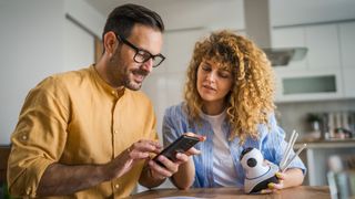 Man and woman looking at smartphone while setting up security camera