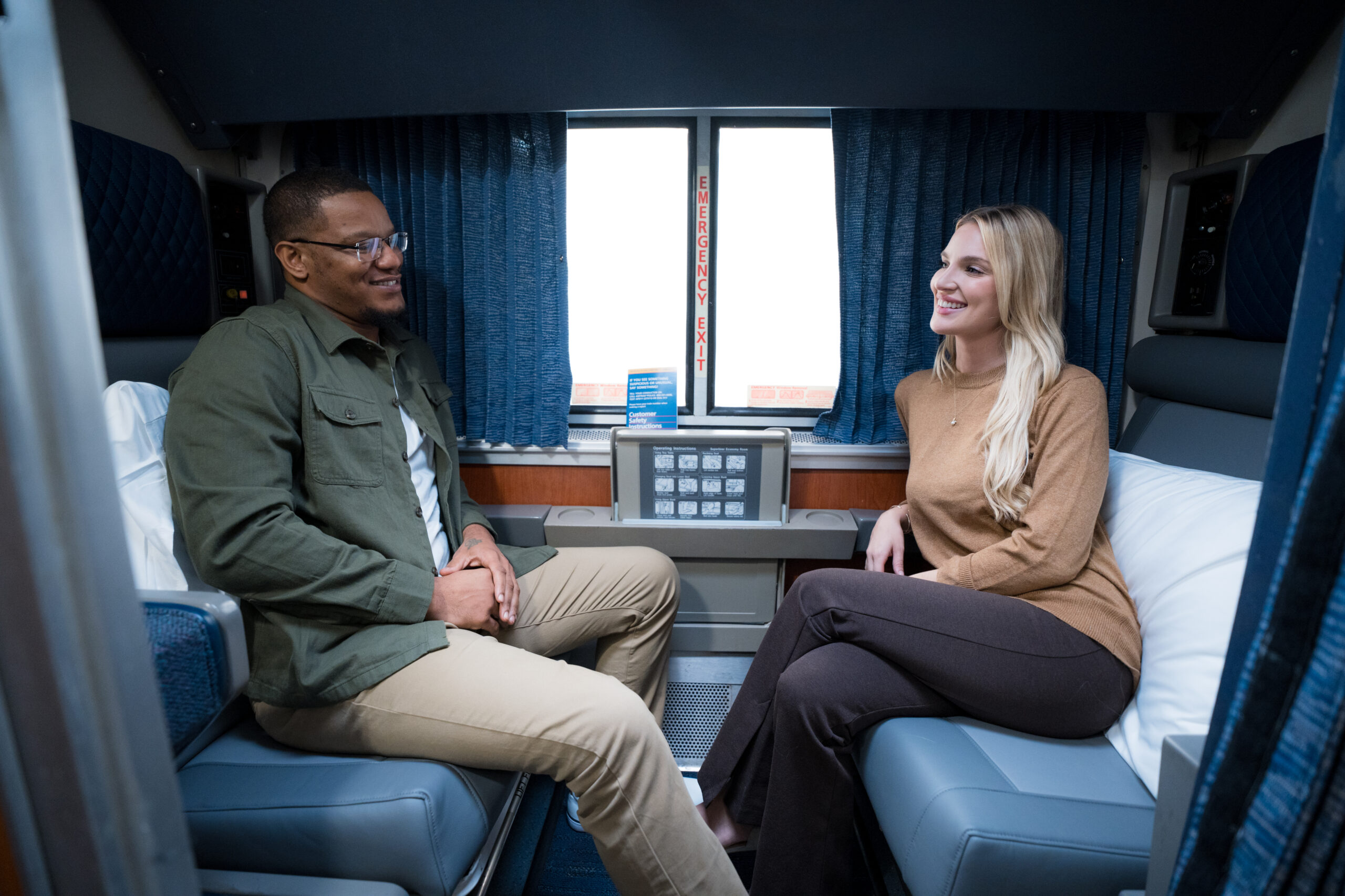A man and a woman face each other on seats in a roomette on an Amtrak train