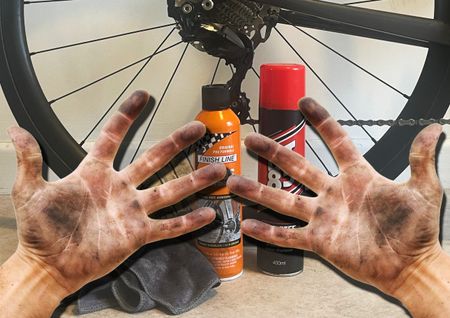 Oily hands with a bicycle wheel and cleaning products in the background