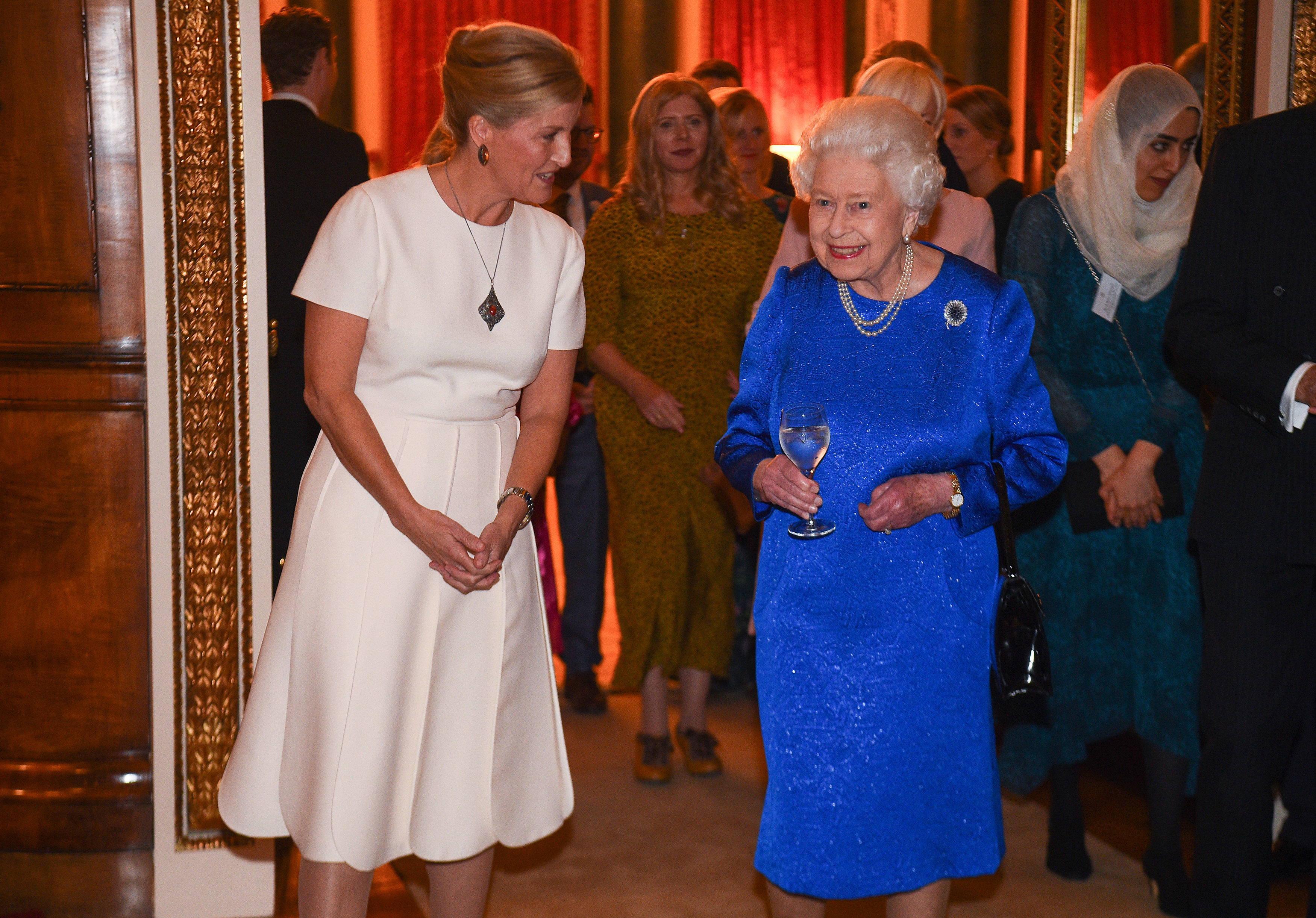 Queen Elizabeth in a blue dress and Duchess Sophie in a white dress smiling at a reception in 2019