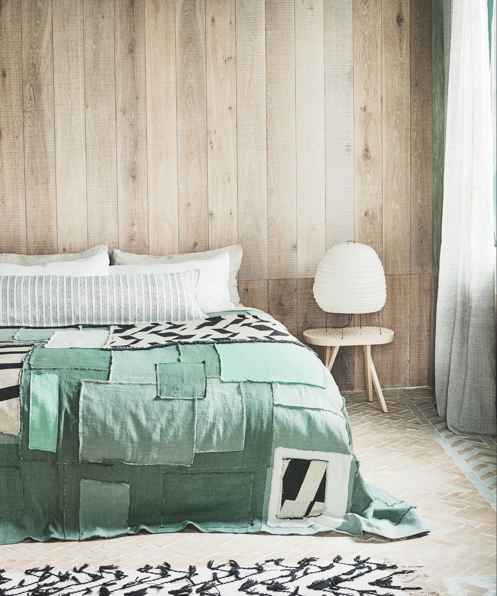 Bedroom with wood clad wall, double bed with green patchwork bedspread, wooden flooring and black and white rug.