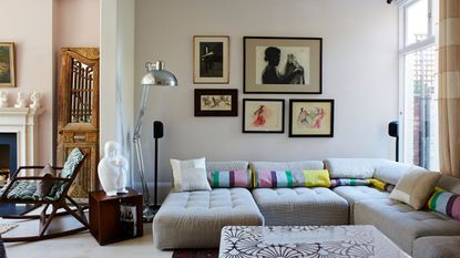 Living room with sectional sofa, drawings on walls, silver floor lamp, antique furniture and coffee table