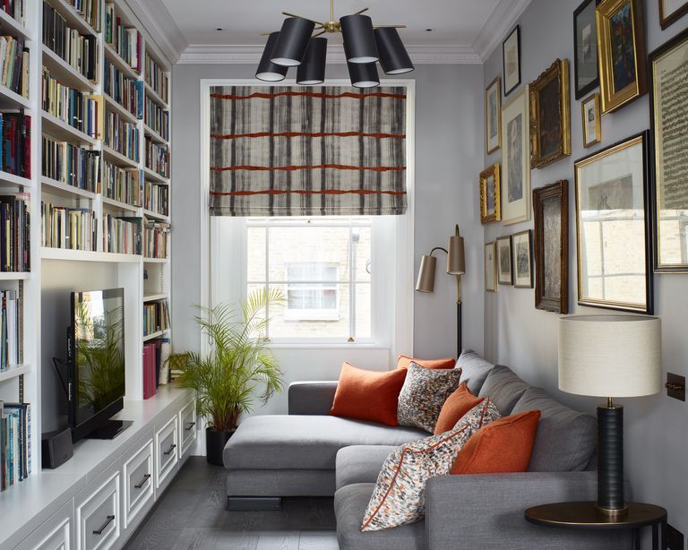 Small living room lighting with a TV nook with grey walls, grey sofa, orange cushions, bookshelf walls, chandelier with black lampshades and floor and table lamps in both corners