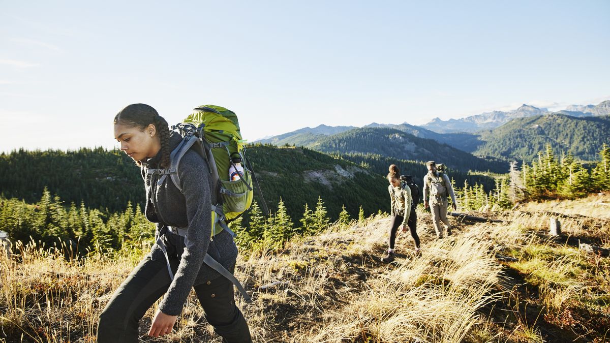 Three woman hike up a trail with the mountains in the background