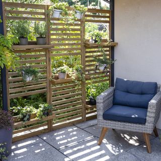 Slatted fencing with shelving attached on patio with potted plants and cushioned chair