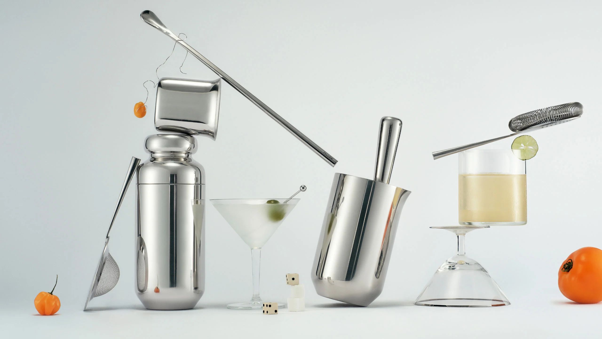 A set of stainless steel barware balanced on top of one another with an array of cocktail glasses and small fruits.