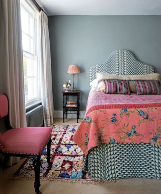 Blue bedroom with pink patterned bed, colorful rug, cream carpet