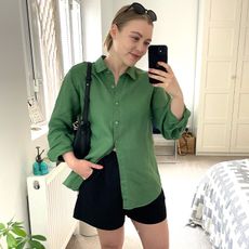 Woman wears green shirt, black shorts, carries bag and sunglasses