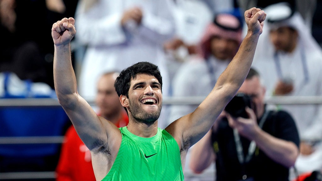 Carlos Alcaraz raises both arms aloft after winning a tennis.
