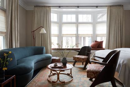 large bedroom with a curved blue sofa and round coffee table at the end of a big white bed