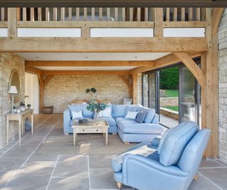 inside of oak frame extension living area with walls, exposed oak beams, tiled floor and pale blue sofas