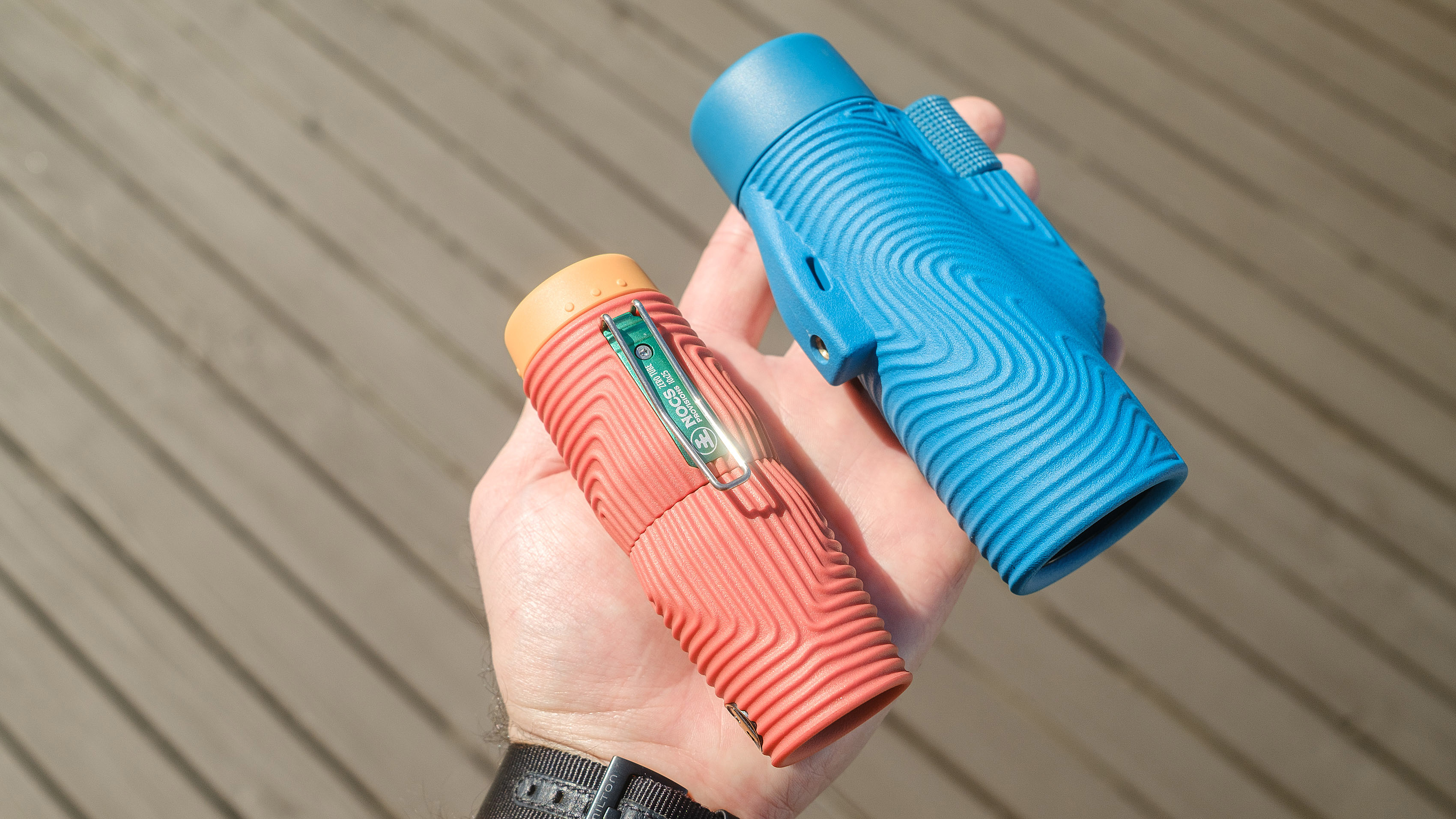 Nocs Zero Tube rugged monocular in orange shown close-up in a user's hand next to the Nocs Zoom Tube in blue