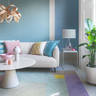 A pastel-coloured living room with a colour-blocked wall and rug and a cream boucle sofa with contrasting cushions