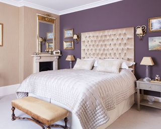 Bedroom with a dark purple feature wall, double bed with llarge bedhead and fireplace with ornate over mantel mirror.