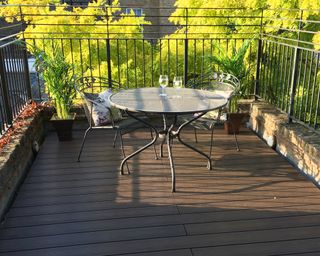 Decking on balcony by Envirobuild with round metal table and two metal chairs and chilled glasses of white wine