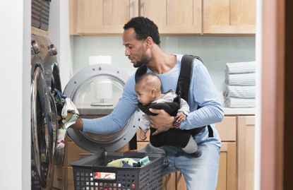 father with son in baby carrier doing laundry