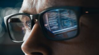 A man wearing glasses with computer code reflected in the glass
