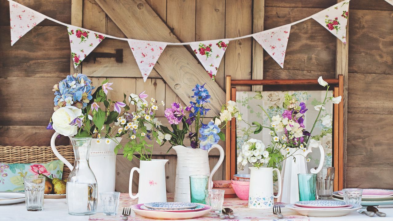 An outdoor dining set with vases of flowers and a bunting behind it