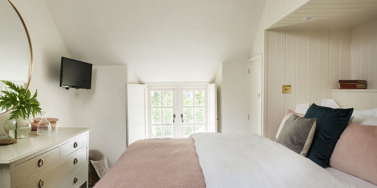 White bedroom with bed in panelled alcove opposite round mirror