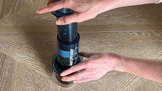 Plunger being pushed down on an AeroPress with coffee filtering into a clear mug