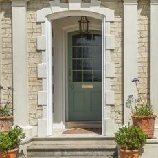 A front porch with a sage green front door and a pendant light