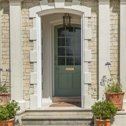 A front porch with a sage green front door and a pendant light