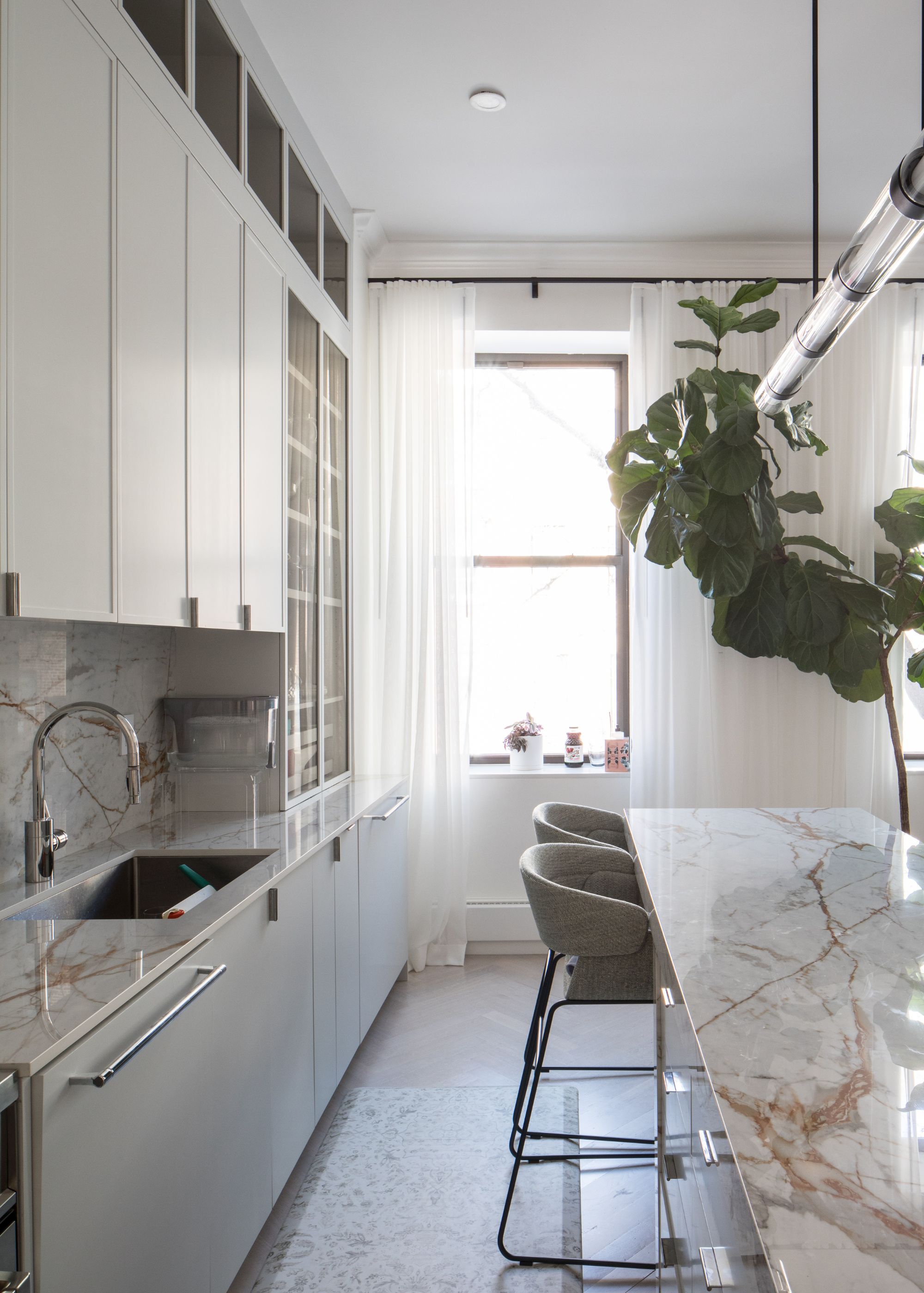 A white kitchen with gold and white marbling on the worktops. A fiddle leaf fig tree is placed in the kitchen to add a pop of color.