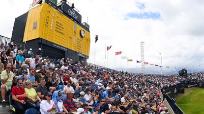 Fans in a grandstand below the big yellow Open scoreboard at the 2025 Open