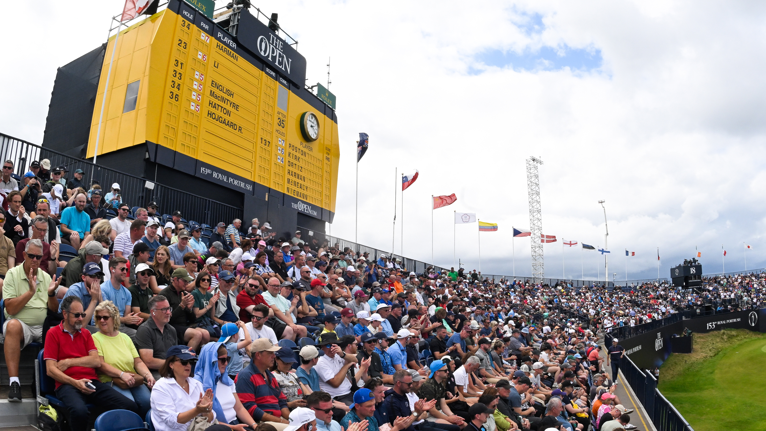 Fans in a grandstand below the big yellow Open scoreboard at the 2025 Open