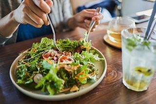 A close p of a person using a knife and fork to eat a salad