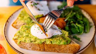 person eating a poached egg on toast with avocado